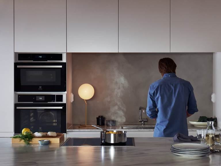 Electrolux uunit ja keittotasot Electrolux uuni ja keittotaso sijoitettuna keittiökalusteisiin. Taka-alalla mies selin laittamassa ruokaa