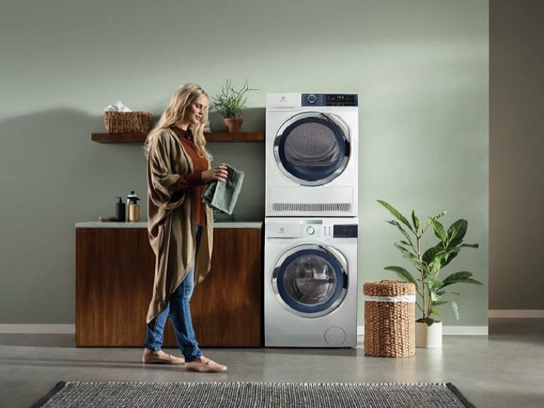 Electrolux pyykinpesu- ja kuivaus Electrolux pyykinpesukone ja kuivausrumpu päällekkäin huoneessa. Vieressä nainen viikkaamassa pyykkiä