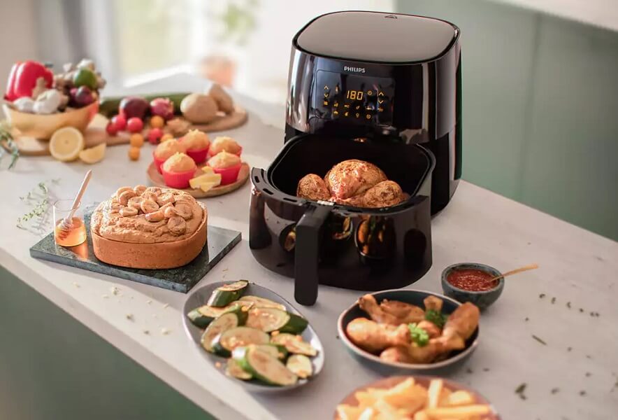 Philips AirFryerit ruoanlaittoon Philips AirFryer asetettuna pöydälle avoimena. AirFryerin sisällä ja ympärillä useita erilaisia aterioita
